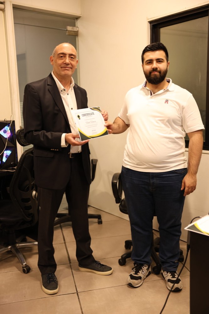 Fadi Tuffaha handing a printed certificate of completion to a participant, the two of them standing side by side at the end of a session.