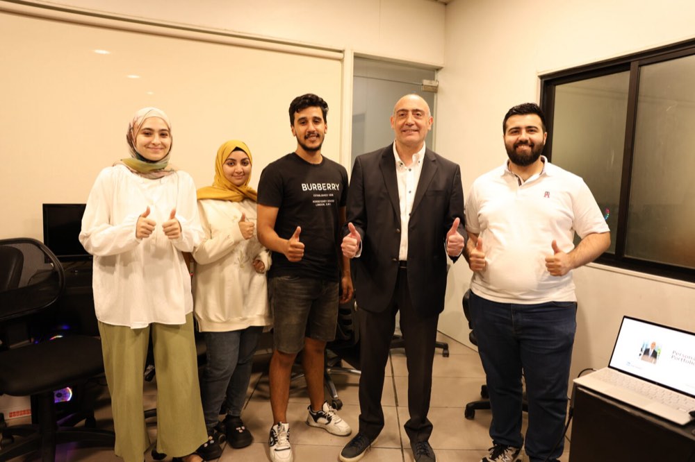 Fadi Tuffaha and five participants standing together at the end of a session, all giving a thumbs up, in the training room.